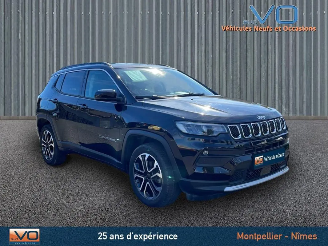 Jeep Compass noir en 3/4 avant droit, avec barres de toit et jantes 18 pouces visibles sur sol goudronné.