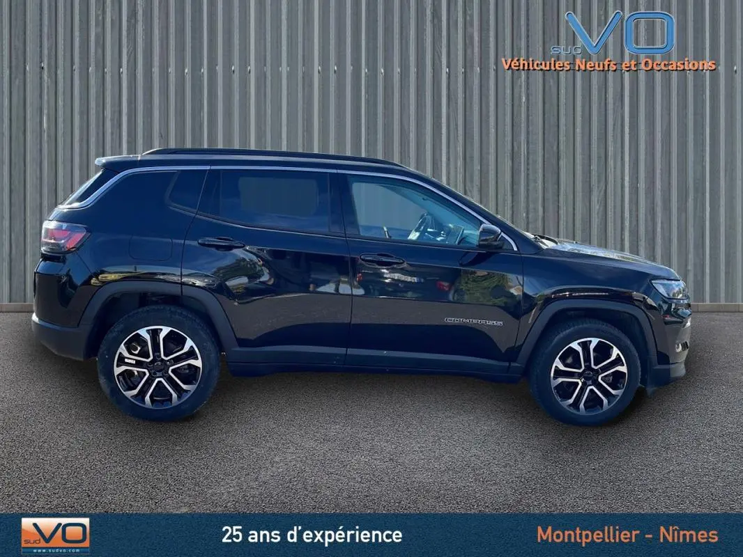 Profil côté gauche d'un Jeep Compass noir 2023 avec jantes 18 pouces et barres de toit visibles sur fond urbain.