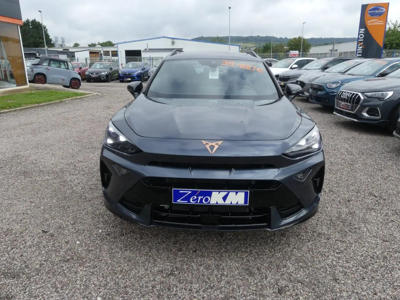 Vue frontale d'un CUPRA Formentor gris Graphene avec logo cuivré et phares LED allumés sur un parking.