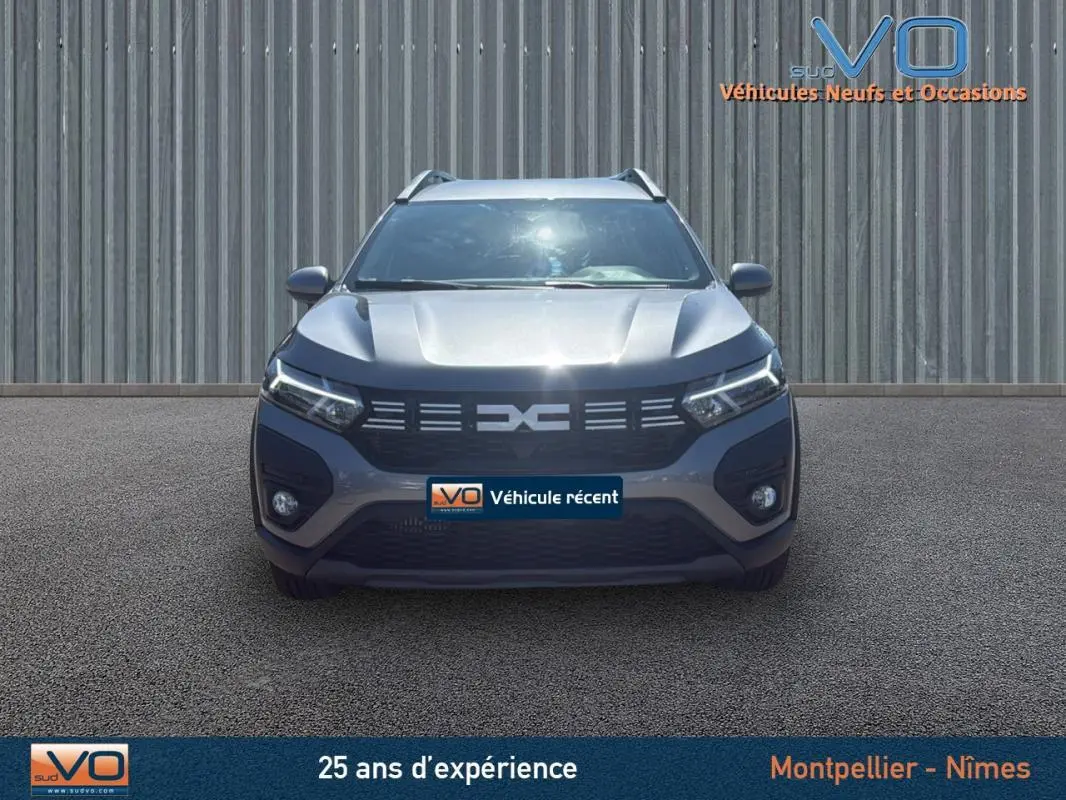 Vue frontale d'un Dacia Jogger gris 2025 avec barres de toit et feux diurnes LED allumés.
