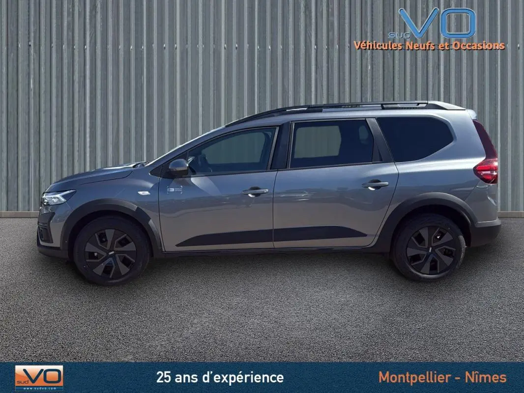 Profil latéral droit d'un Dacia Jogger gris 2025 avec barres de toit et jantes noires distinctives.