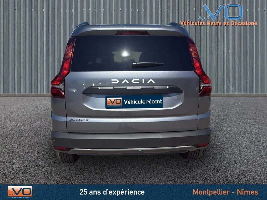 Vue arrière d'un Dacia Jogger gris 2025 avec feux verticaux et logo bien visibles sur fond urbain.