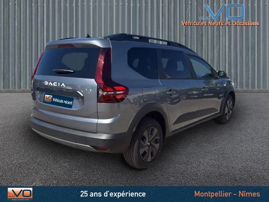 Vue 3/4 arrière droite d'un Dacia Jogger gris 2025 avec barres de toit et feux arrière caractéristiques.