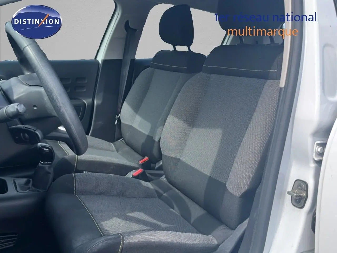Vue intérieure côté conducteur de la Citroën C3 blanche 2018, montrant les sièges en tissu gris et la boîte manuelle.