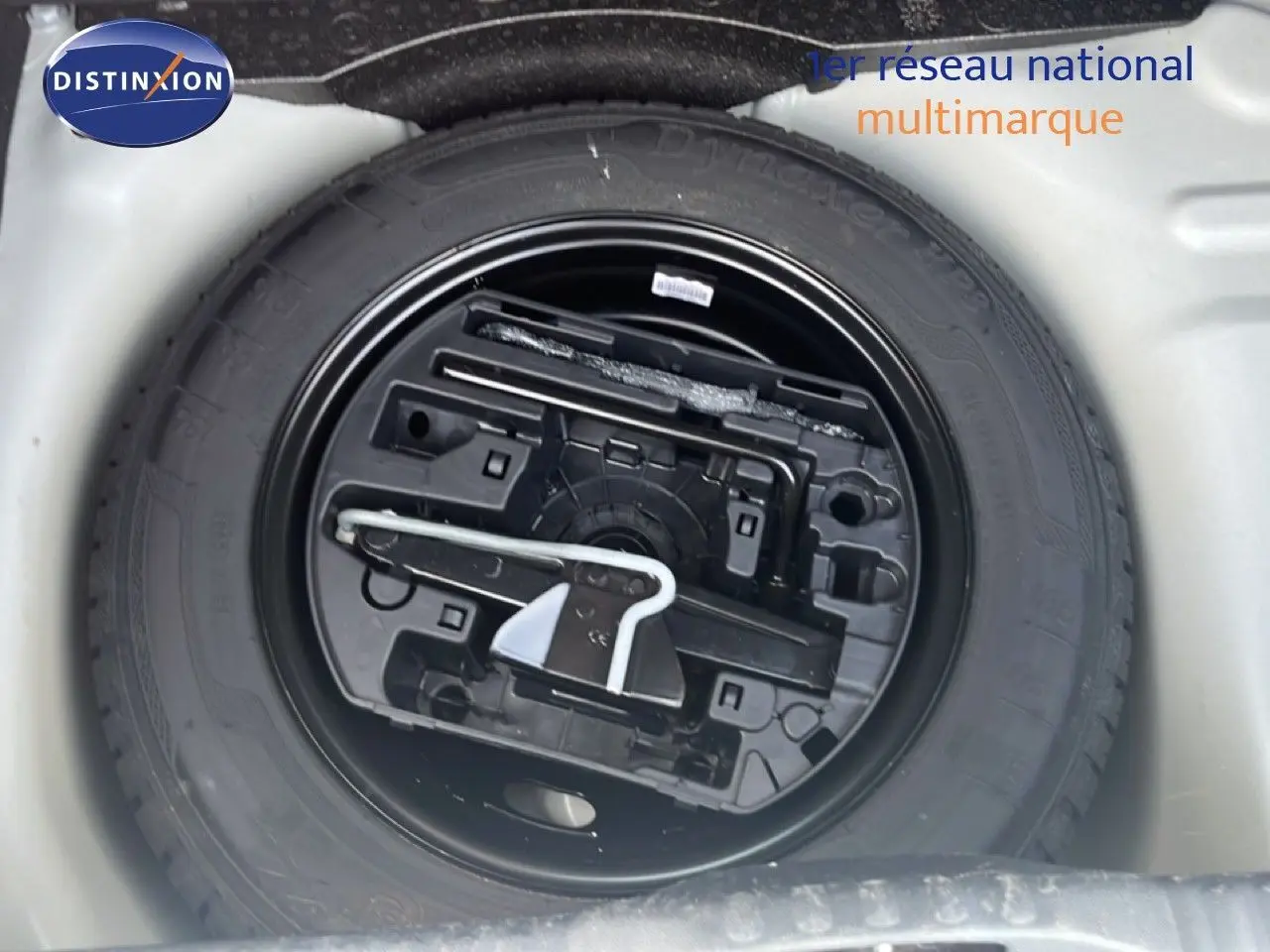 Roue de secours noire avec outillage intégré, vue en plongée dans le coffre d'une Citroën C3 blanche 2018.