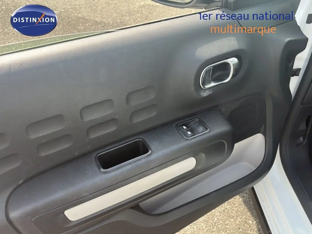 Vue rapprochée de la porte avant droite blanche d'une Citroën C3 2018 avec poignée intérieure chromée et commande de vitre.
