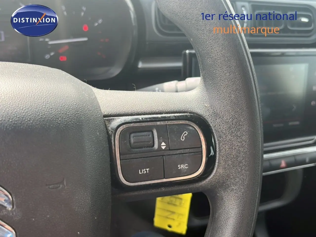 Gros plan sur les commandes au volant noir d'une Citroën C3 blanche, avec tableau de bord et écran tactile en arrière-plan.