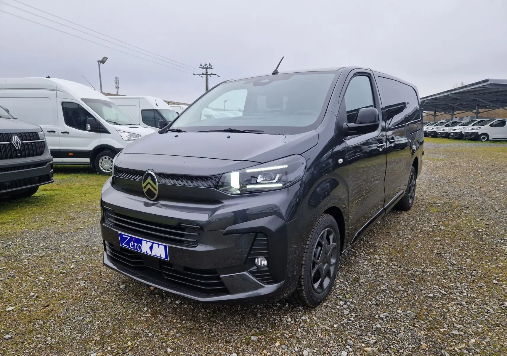 Vue 3/4 avant droit d'un Citroën Jumpy Cabine Approfondie gris titane avec feux LED allumés sur un parking extérieur.