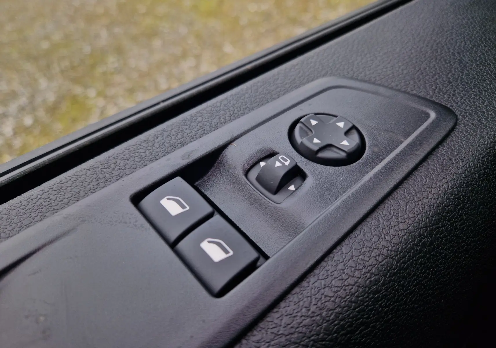 Gros plan sur les commandes de réglage des rétroviseurs et vitres côté conducteur du Citroën Jumpy Gris Titane, intérieur noir.