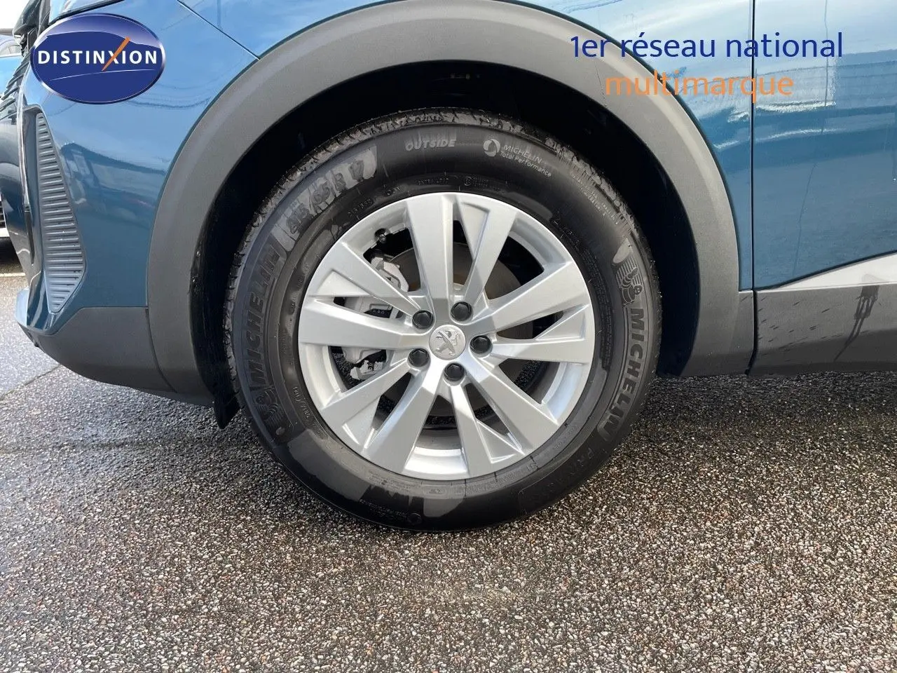 Gros plan sur la roue avant gauche d'un Peugeot 3008 bleu Célèbes Métal avec jante alliage argentée.