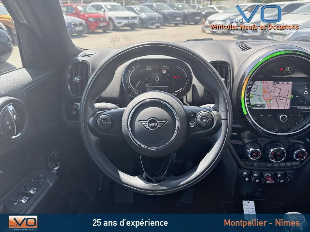 Vue intérieure centrée sur le volant sport MINI avec tableau de bord numérique et écran tactile de navigation allumé.