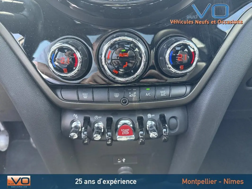 Gros plan sur la console centrale de la MINI Countryman gris clair, avec commandes de climatisation et bouton start/stop rouge.