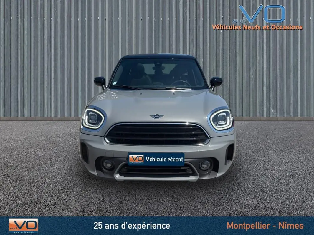 Vue frontale d'une MINI Countryman gris clair avec phares LED allumés et calandre noire, sur fond industriel.