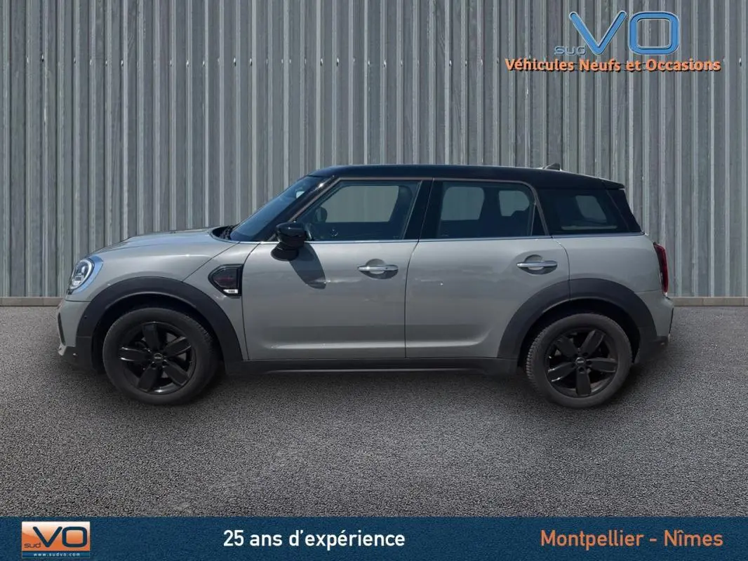 Profil côté gauche d'une MINI Countryman gris clair avec toit noir et jantes alliage noires sur fond urbain.