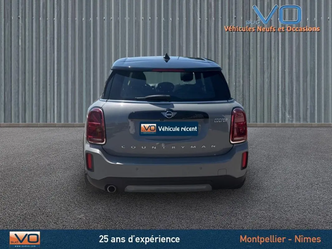 Vue arrière d'une MINI Countryman gris clair avec feux rouges et toit noir sur fond urbain neutre.