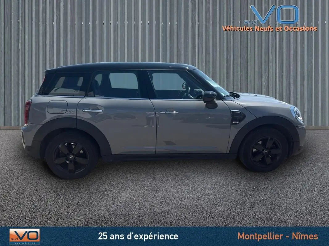 Profil côté gauche d'une MINI Countryman gris clair avec toit noir et jantes alliage noires sur fond industriel.