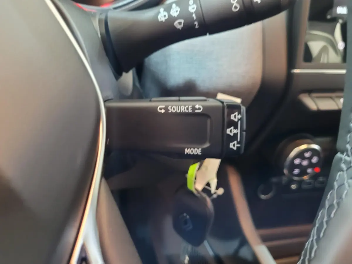 Gros plan sur la commande multimédia au volant d'une Renault Clio gris foncé, montrant les boutons source et mode.