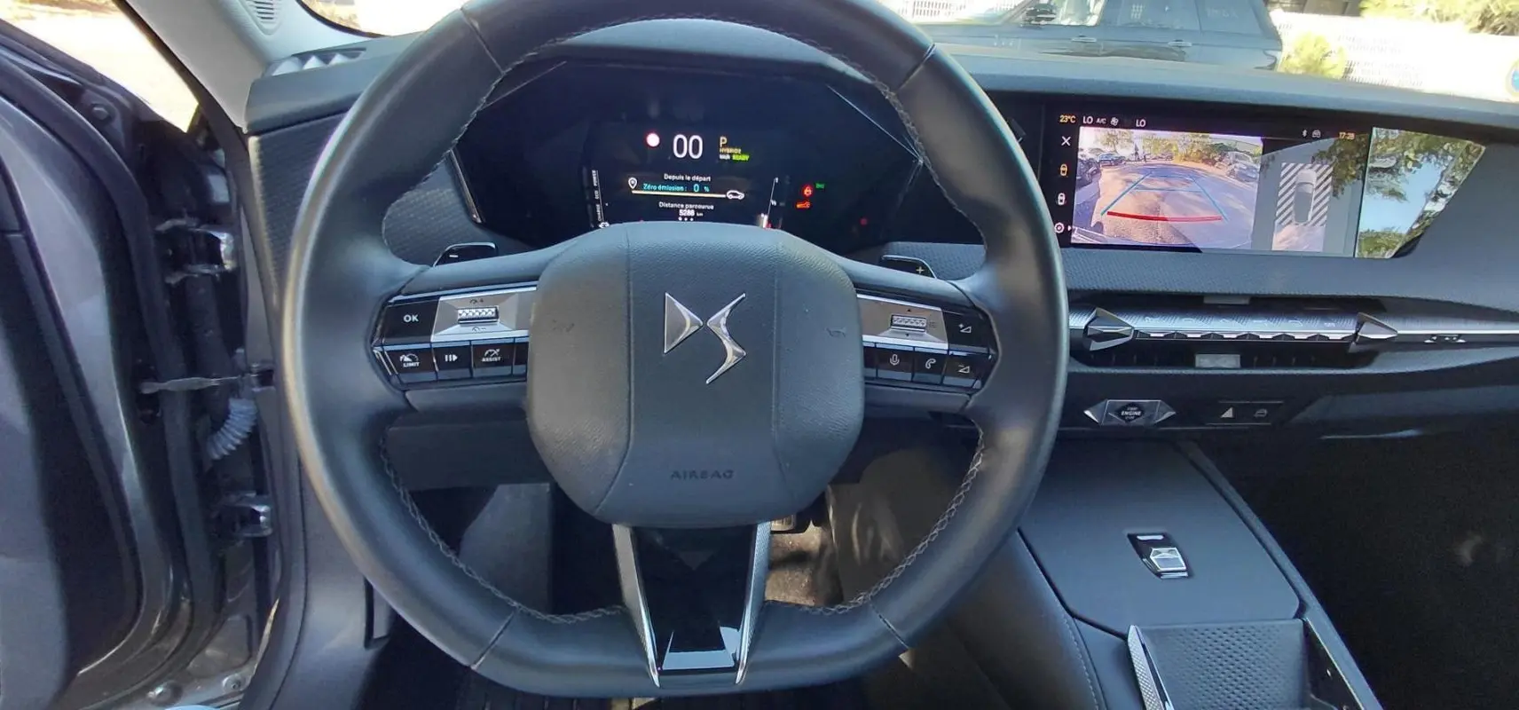 Vue intérieure centrée sur le volant noir du DS4 Hybride 2024, avec tableau de bord numérique et écran tactile affichant la caméra de recul.