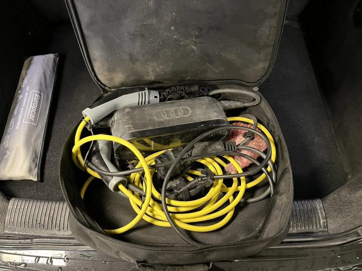 Coffre ouvert d'une Audi A3 noire avec câble de recharge hybride jaune et noir rangé dans un sac noir.