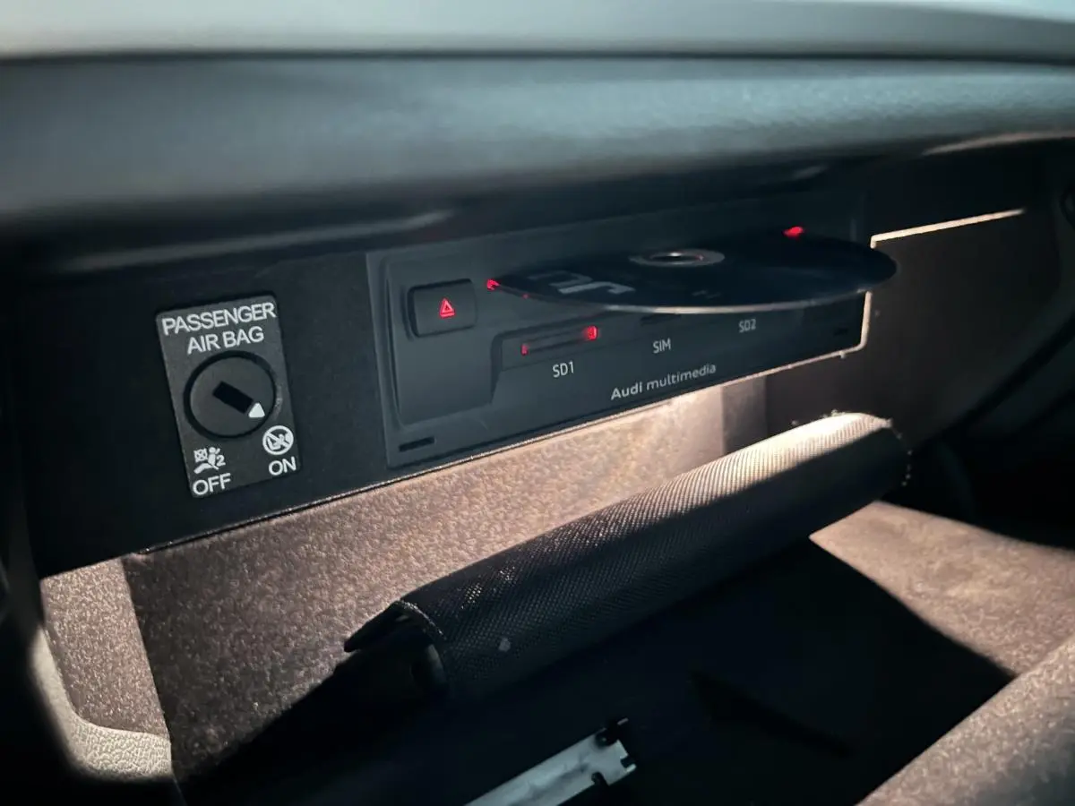 Gros plan sur la boîte à gants ouverte de l'Audi A3 noire, montrant le lecteur Audi multimedia avec un CD inséré.