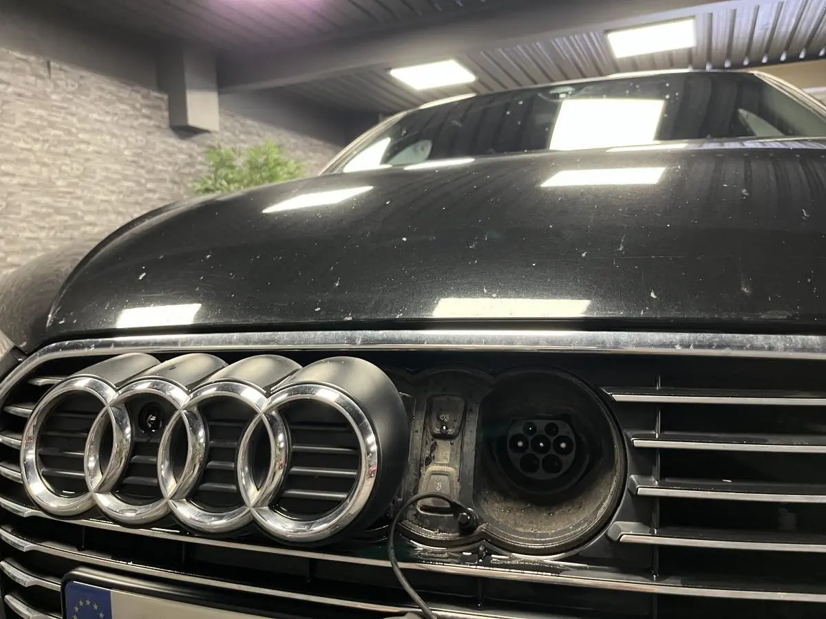 Gros plan sur la calandre avant noire d'une Audi A3 1.4 TFSI e-tron S line avec prise de recharge visible à droite des anneaux.