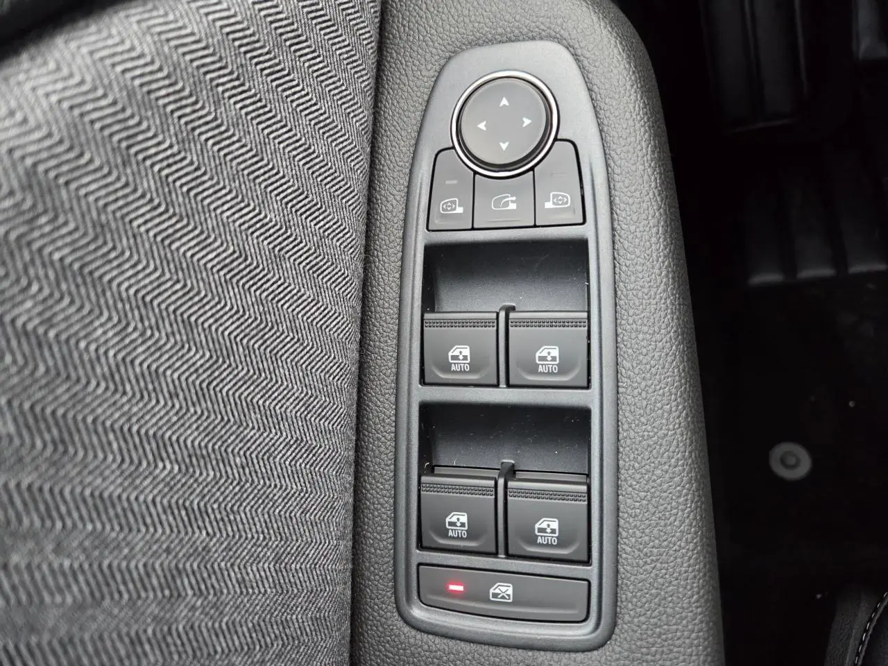 Gros plan sur les commandes des vitres électriques et rétroviseurs, sur la porte côté conducteur avec tissu gris à motif chevrons.