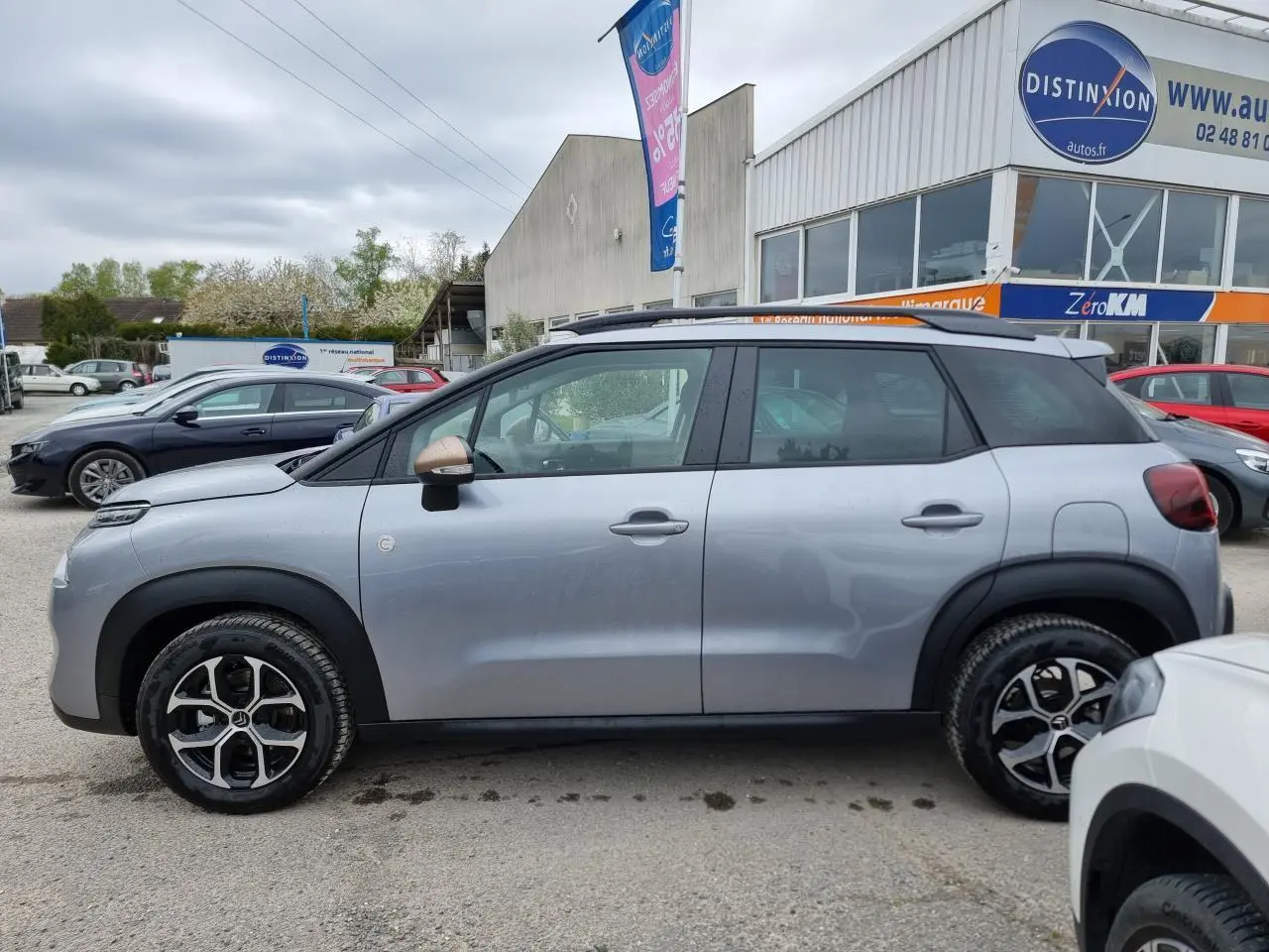 Profil côté gauche d'une Citroën C3 Aircross gris Artence avec jantes alliage diamantées et barres de toit noires.