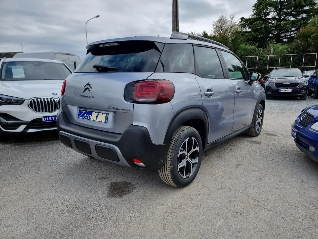 Vue 3/4 arrière droite d'un Citroën C3 Aircross gris Artence avec jantes alliage et barres de toit noir brillant.