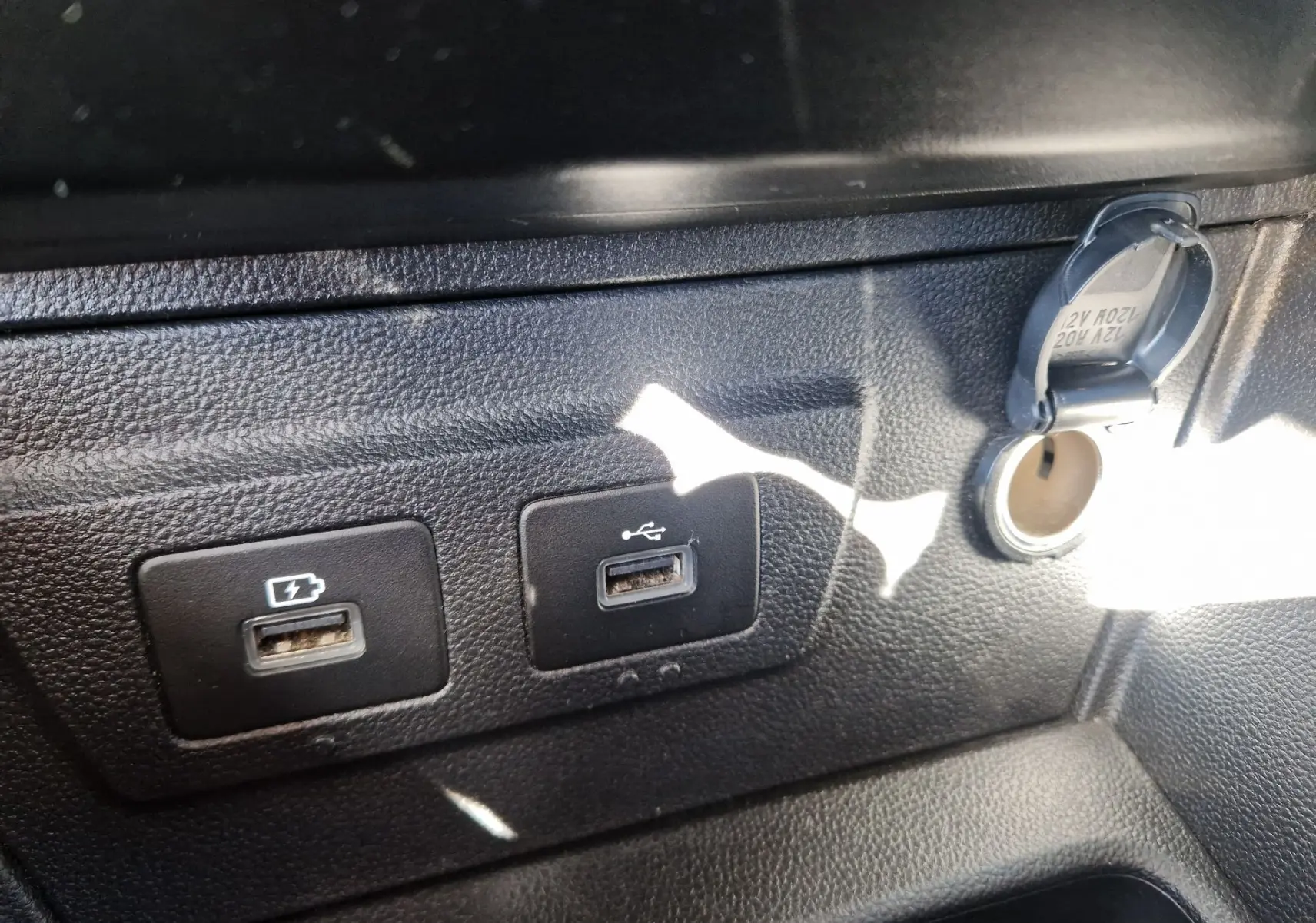 Gros plan sur les ports USB et prise 12V du tableau de bord noir du Dacia Duster blanc 2024.