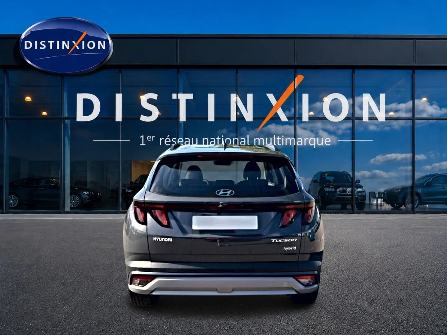 Vue arrière d'un Hyundai Tucson gris ecotronic 2026 hybride garé devant une vitrine avec logo Distinxion.