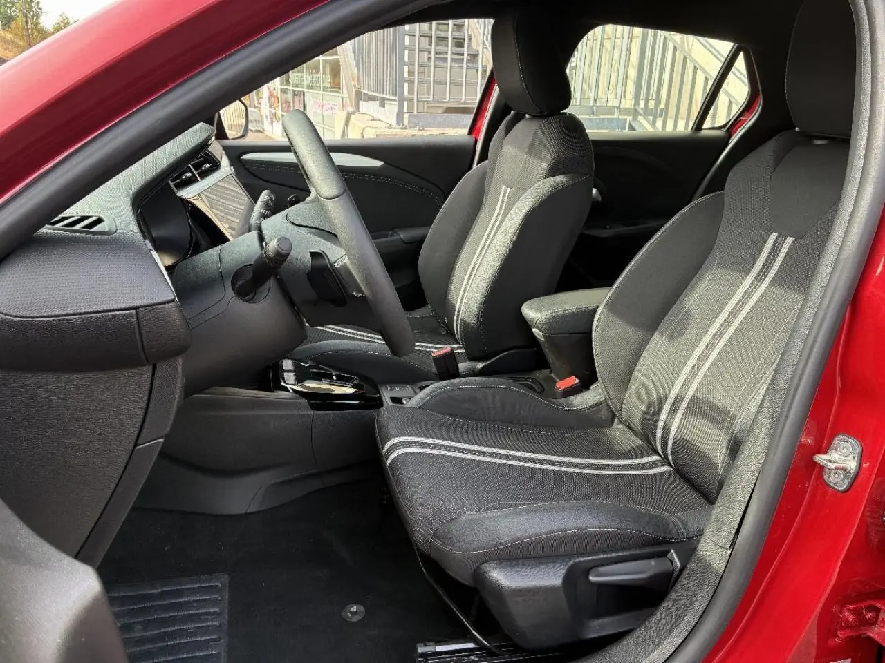Vue intérieure côté conducteur de l’Opel Corsa 2025 rouge peperoncino, montrant les sièges noirs avec surpiqûres claires.