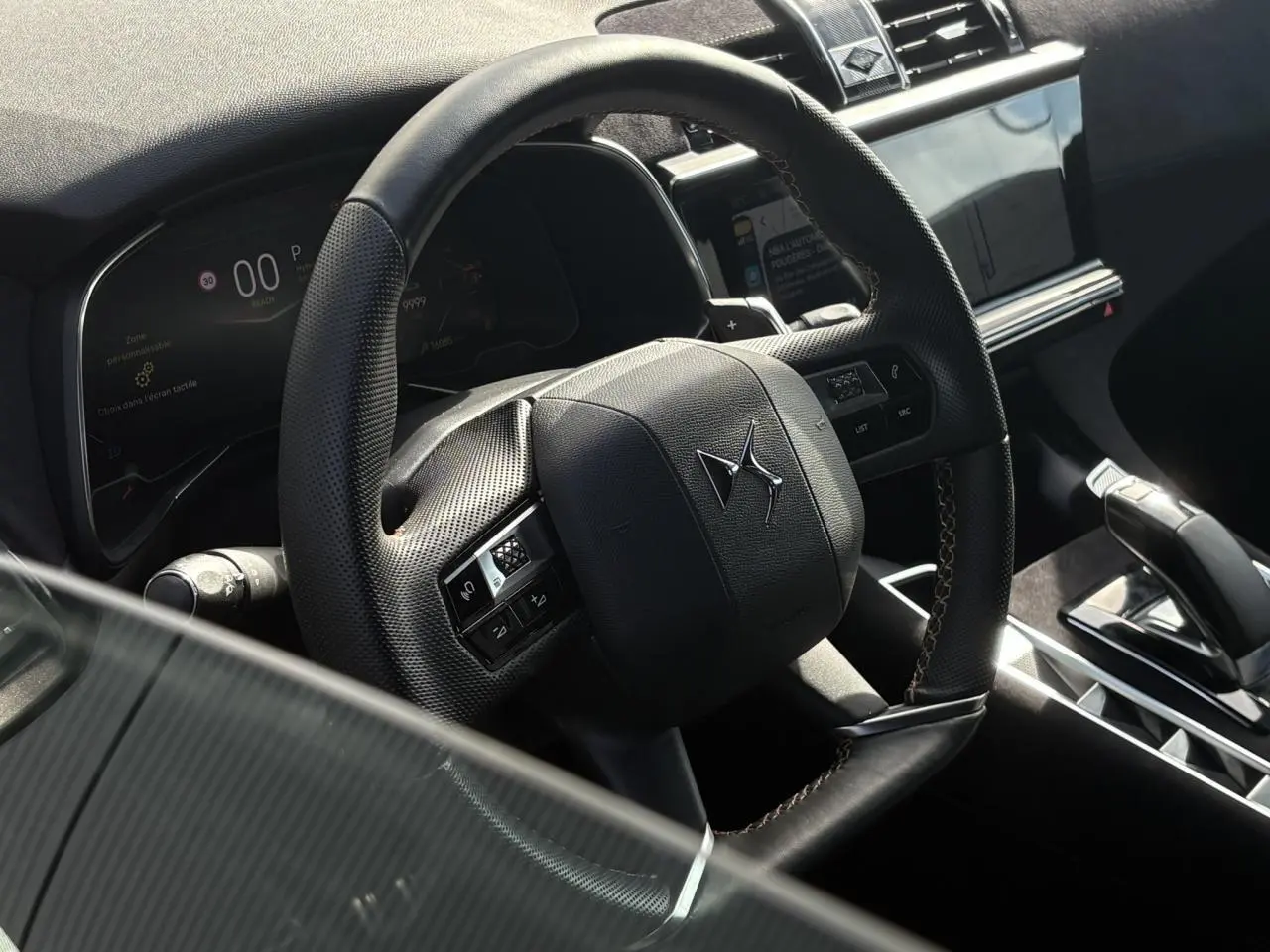 Vue rapprochée du volant en cuir noir perforé avec surpiqûres Carmin et Or du DS7 2024, tableau de bord et écran tactile visibles.