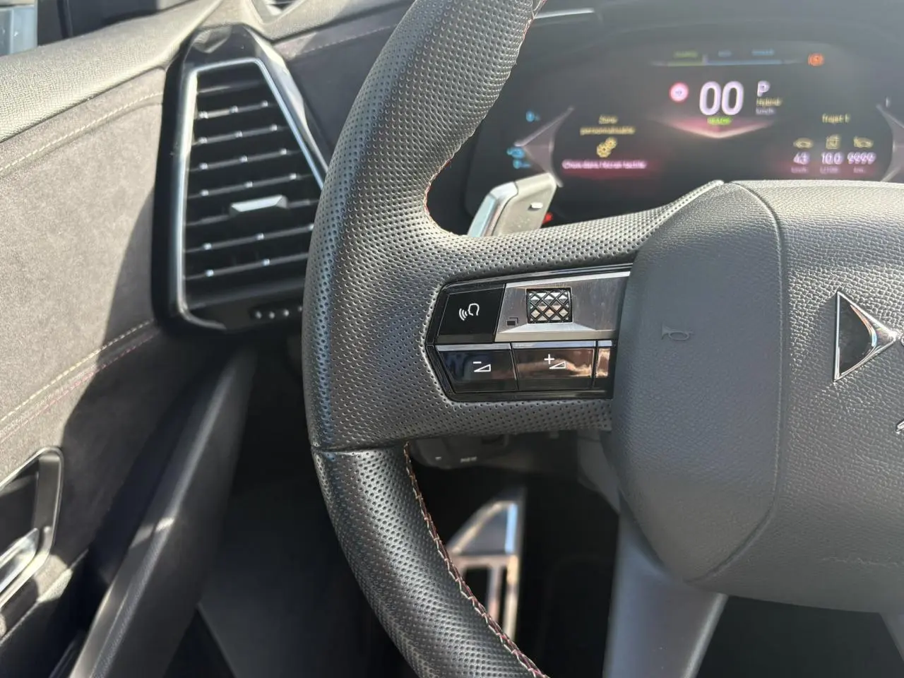 Gros plan sur le volant perforé noir avec surpiqûres Carmin et Or du DS7 1.6 E-Tense 2024, tableau de bord numérique en arrière-plan.