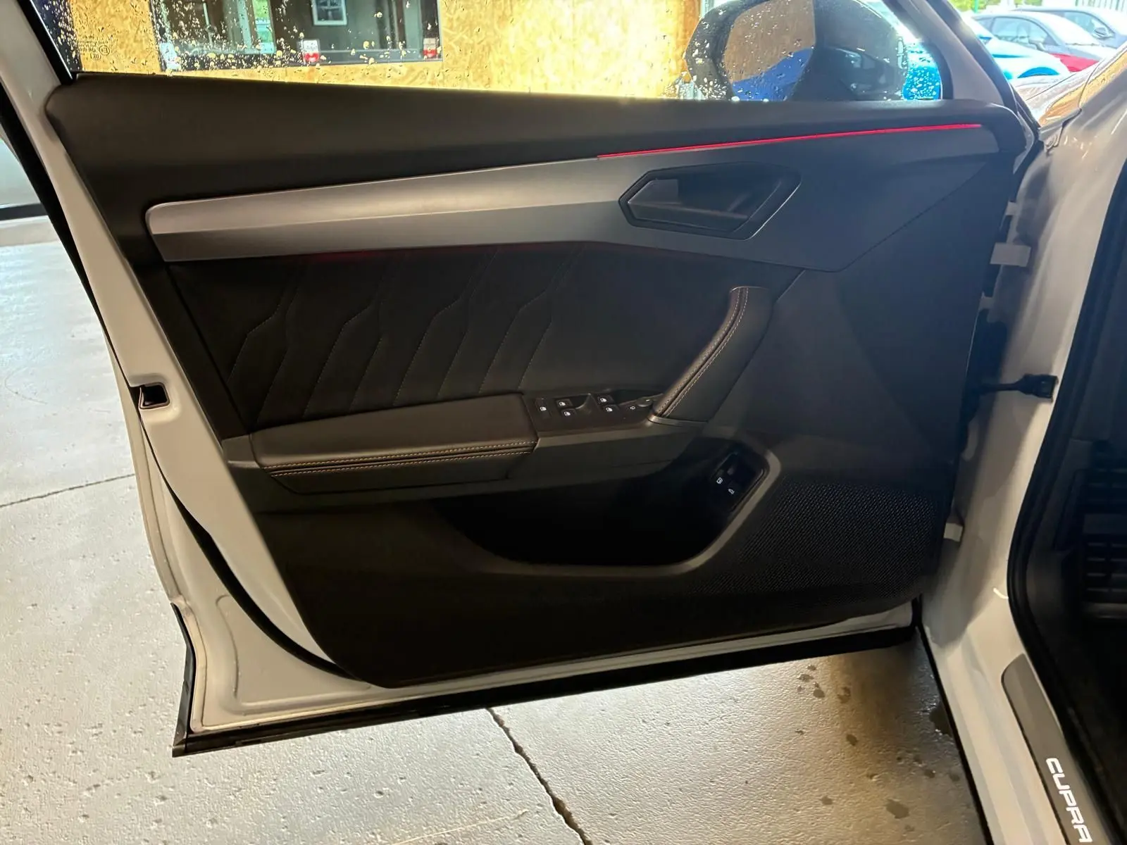 Vue intérieure de la porte avant gauche grise du CUPRA Formentor 1.4 E-HYBRID 2024 avec éclairage d'ambiance rouge.