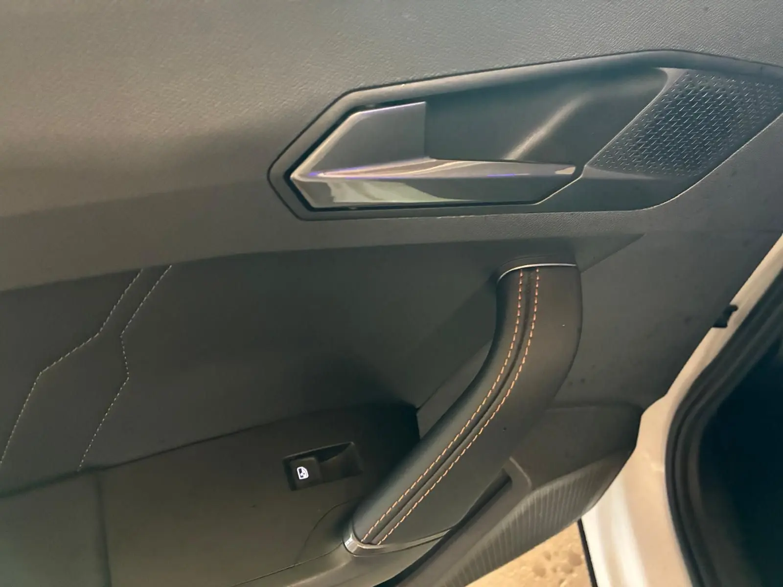 Poignée de porte intérieure avec surpiqûres orange sur tissu noir, côté gauche d'une CUPRA Formentor gris 2024.
