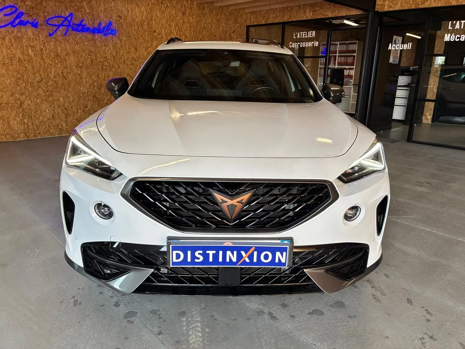 Vue avant d'une CUPRA Formentor blanche 2024 avec calandre noire et logo CUPRA cuivré, en intérieur showroom.