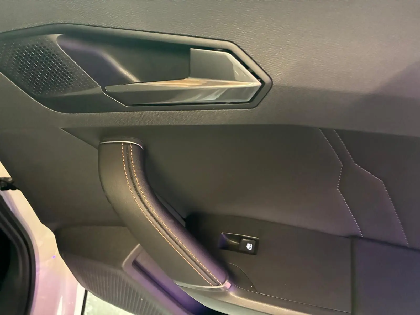 Poignée de porte intérieure côté gauche de la CUPRA Formentor gris, avec surpiqûres orange et bouton de verrouillage.