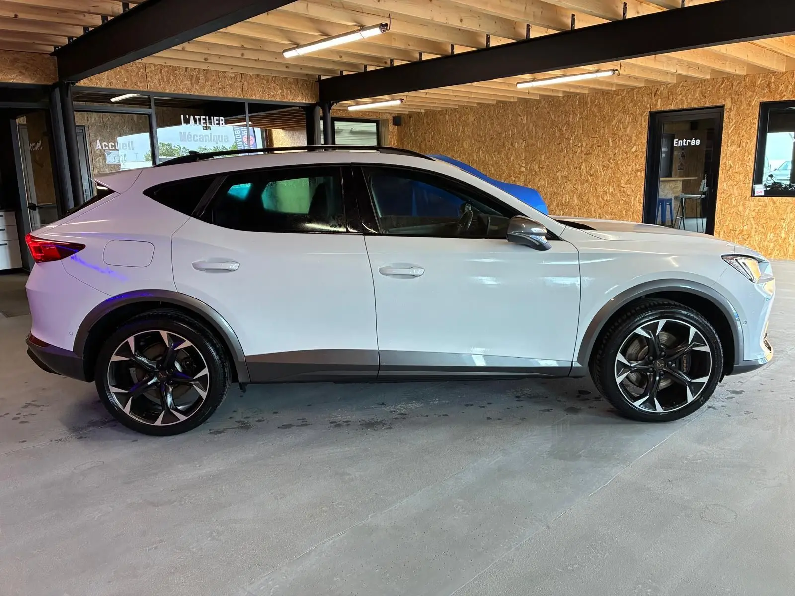 Vue de profil côté gauche du CUPRA Formentor gris 2024 avec jantes noires et toit noir dans un garage.