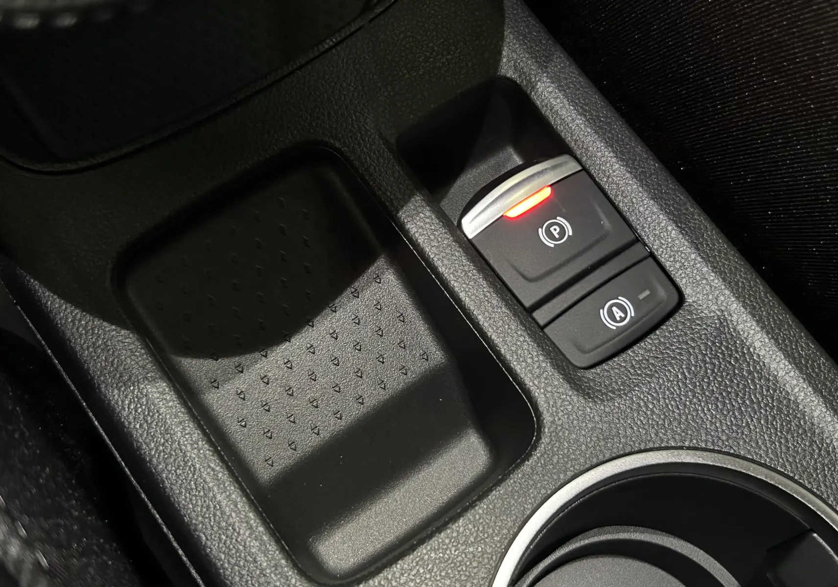Gros plan sur la console centrale noire du Renault Captur II Ph.2, avec bouton de frein à main électronique allumé en rouge.