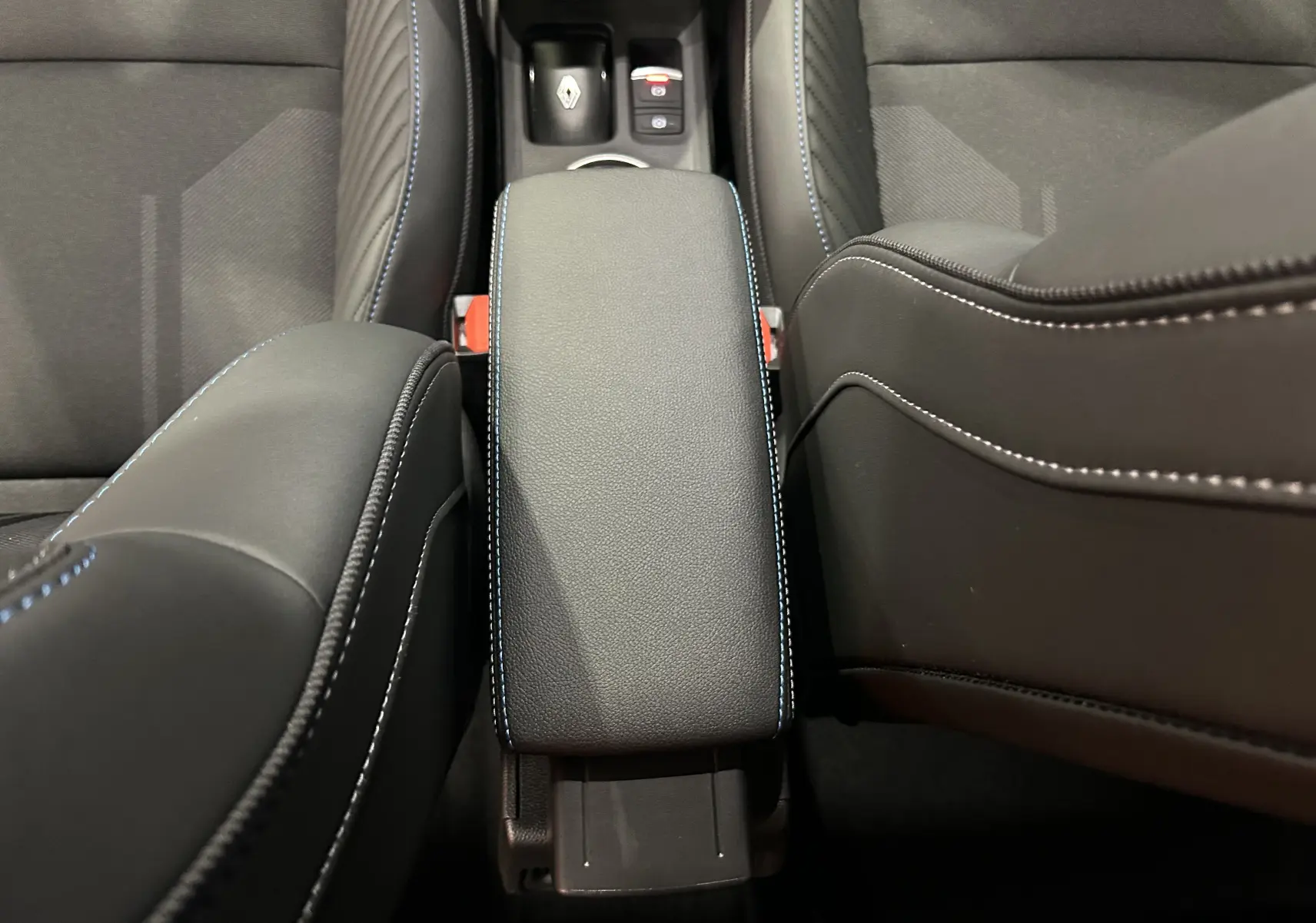 Vue rapprochée de l'accoudoir central en cuir noir avec surpiqûres bleues dans l'habitacle du Renault Captur blanc nacré.