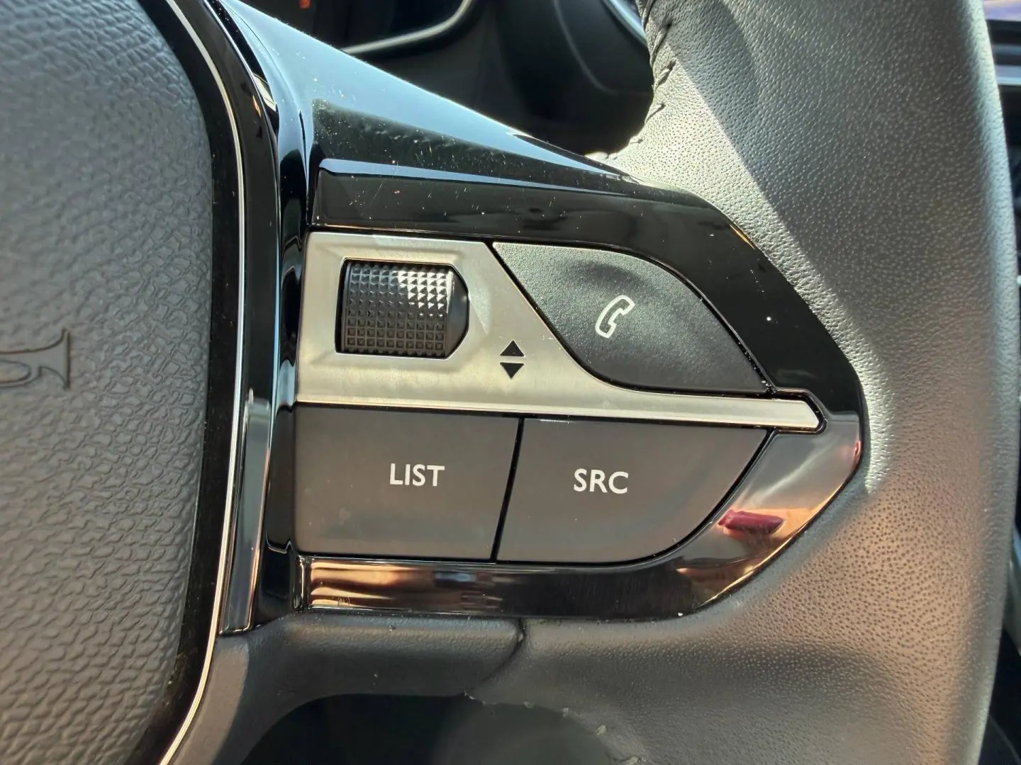 Gros plan sur les commandes noires et argentées du volant côté gauche d’une Peugeot 208 gris Artense 2025.
