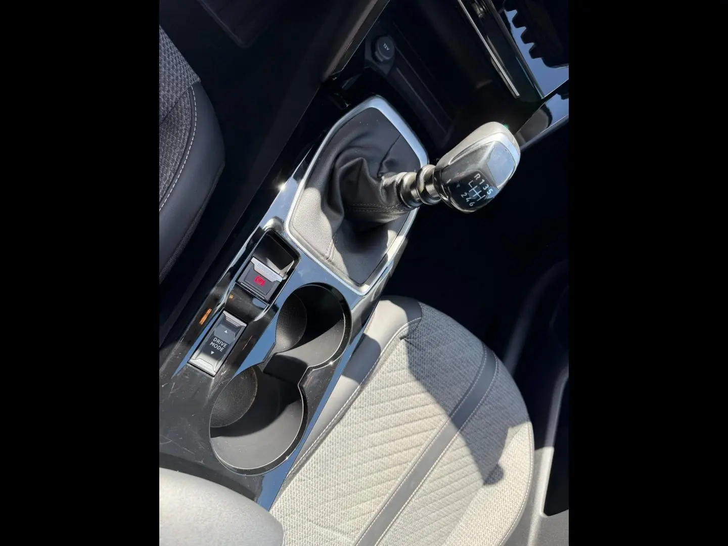 Vue rapprochée de la console centrale de la Peugeot 208 2025 avec levier de vitesse manuel et siège tissu gris clair.