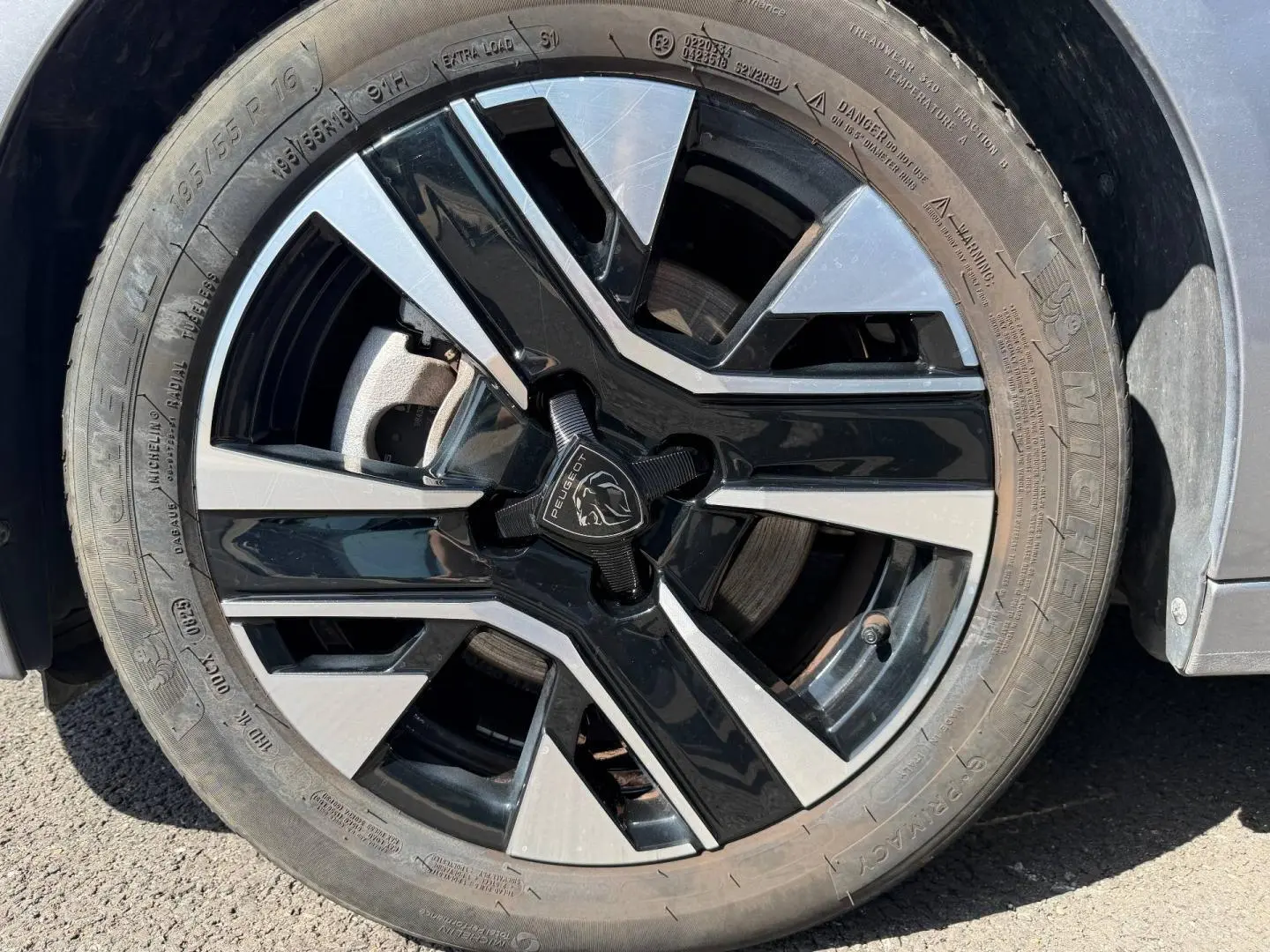 Gros plan sur la jante alu bicolore noire et argentée d'une Peugeot 208 gris Artense, côté avant droit.