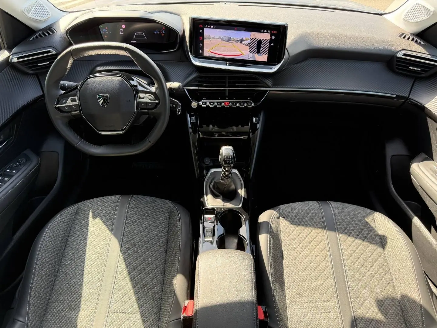 Vue intérieure frontale de la Peugeot 208 1.2 100ch S&S Allure avec tableau de bord noir, écran tactile et sièges tissu gris.