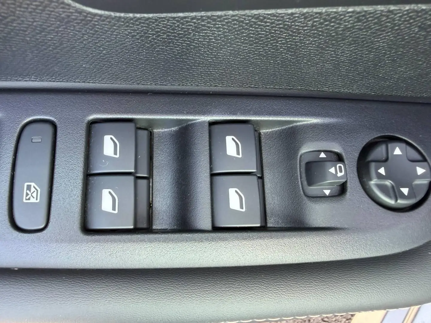 Gros plan sur les commandes électriques des vitres et réglages des rétroviseurs côté conducteur d'une Peugeot 208 gris Artense.