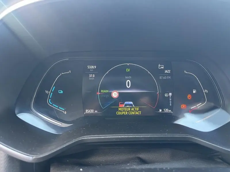 Tableau de bord numérique de Renault Clio 1.6 E-Tech 2021 affichant vitesse, autonomie et alertes moteur en vue frontale.