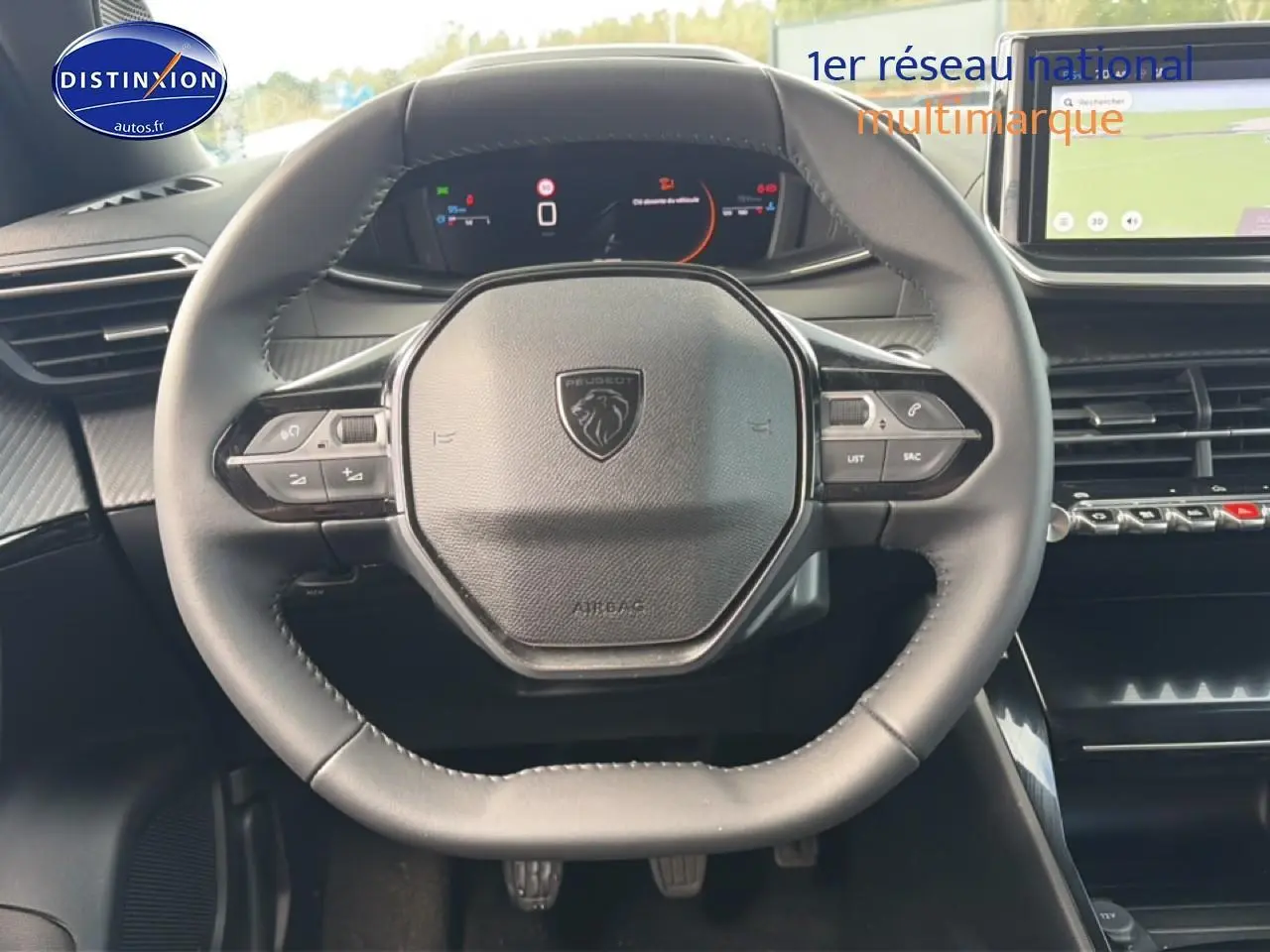 Vue rapprochée du volant noir multifonction de la Peugeot 2008 1.2 100 allure avec tableau de bord digital et écran tactile.