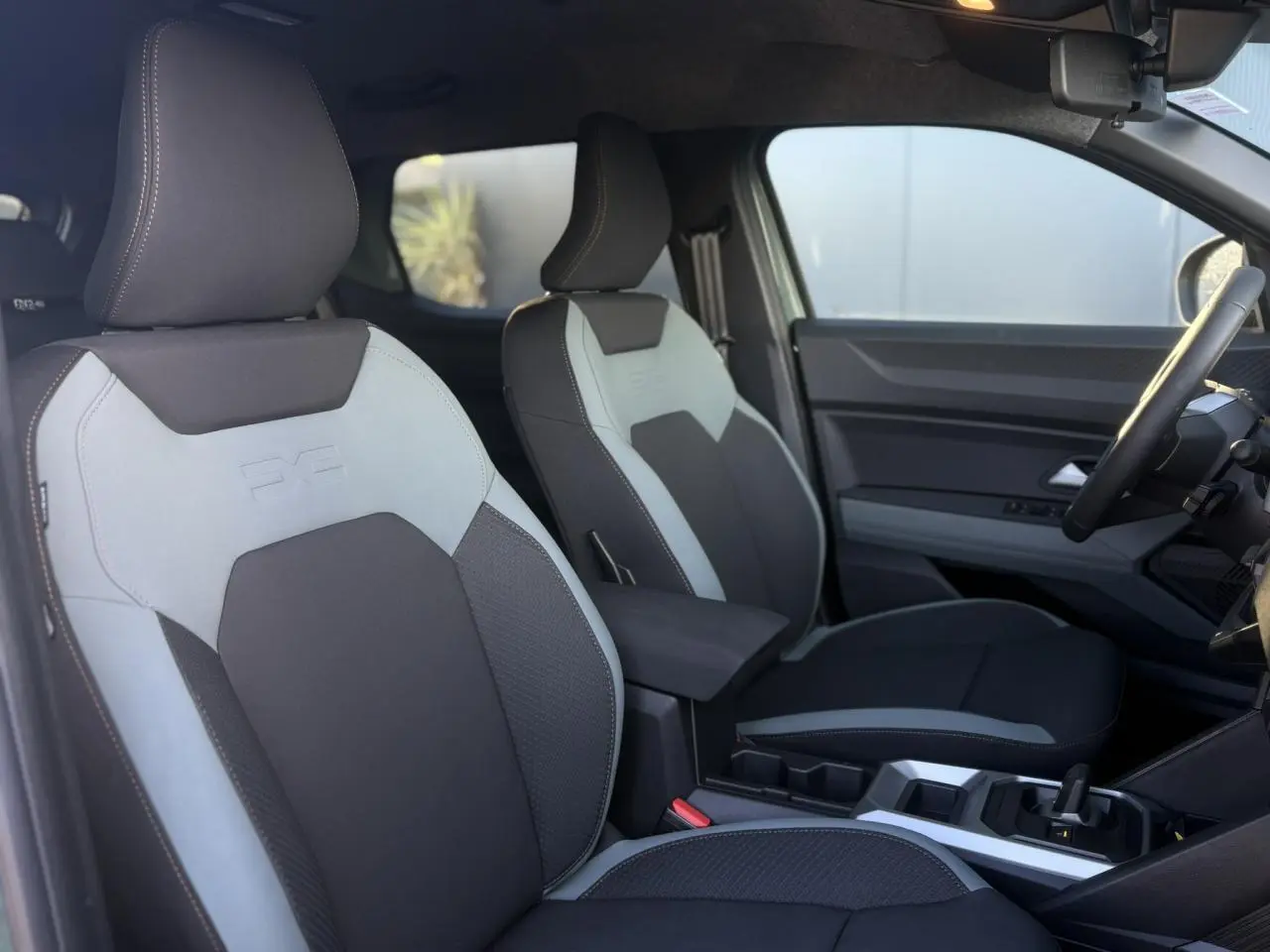 Vue intérieure côté conducteur du Dacia Duster 2026, sièges TEP MicroCloud gris clair et foncé avec accoudoir central.