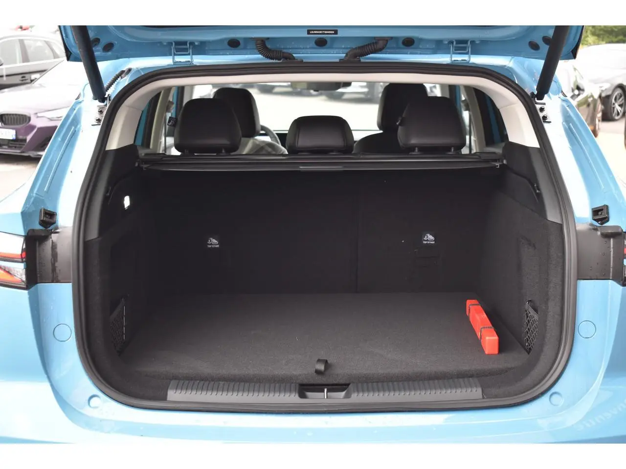 Coffre ouvert vu de l'arrière d'un MG Motor EHS bleu 2026, avec banquette arrière et tapis noir visible.