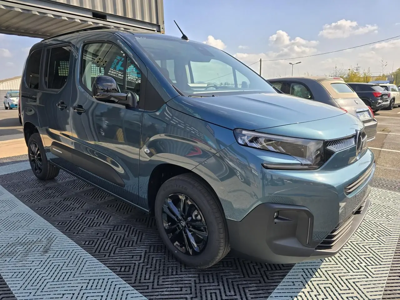 Vue 3/4 avant droite d'un Citroën Berlingo 2025 bleu Kiama métallisé avec jantes aluminium noires et barres de toit.